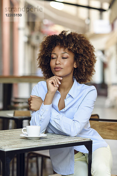 Entspannte Frau mit Afro-Frisur sitzend im Outdoor-Café
