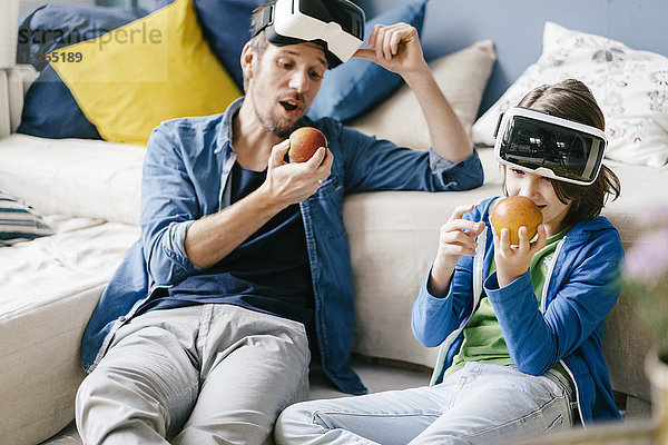 Vater und Sohn mit VR-Brille und Äpfel essen zu Hause