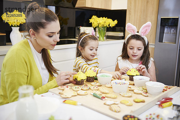 Mutter mit Töchtern  die Osterkekse und Muffins in der Küche dekorieren.