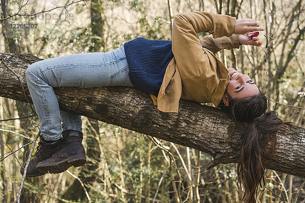 Glückliche junge Frau auf einem Baumstamm in der Natur liegend