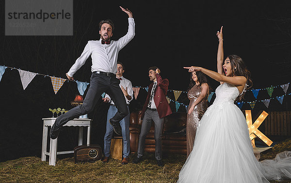 Überraschte Braut schaut auf einen Mann  der mit Freunden auf einer Nachtfeldparty springt.