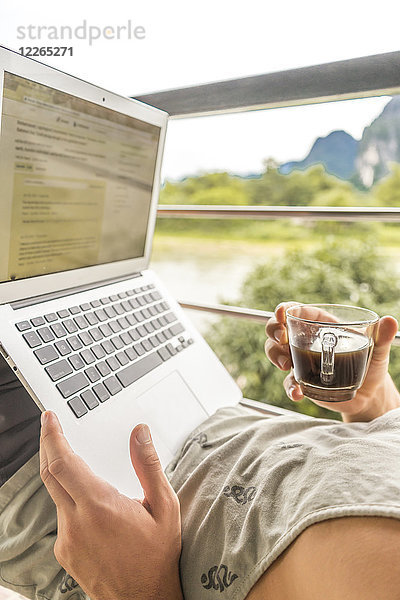 Laos  Vang Vieng  junger Mann mit Laptop in Hängematte liegend  Tee trinkend