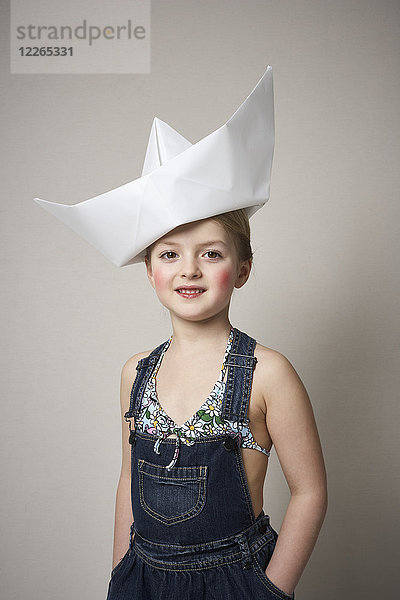 Porträt des kleinen Mädchens mit großem Papierboot auf dem Kopf