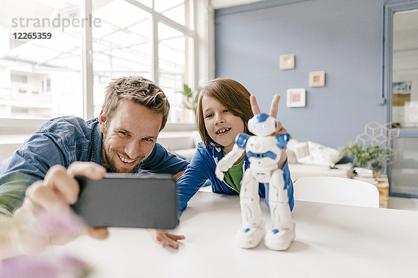 Glücklicher Vater und Sohn nehmen einen Selfie mit Roboter zu Hause mit auf den Tisch