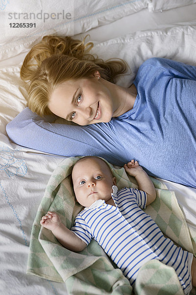 Porträt der lächelnden Mutter mit ihrem kleinen Jungen auf dem Bett liegend