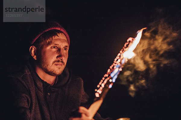Mann mit brennendem Baumstamm bei Nacht