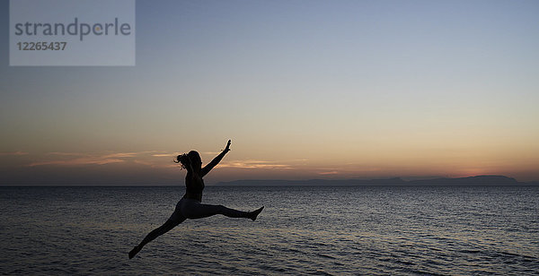 Junge Frau springt bei Sonnenuntergang ans Meer