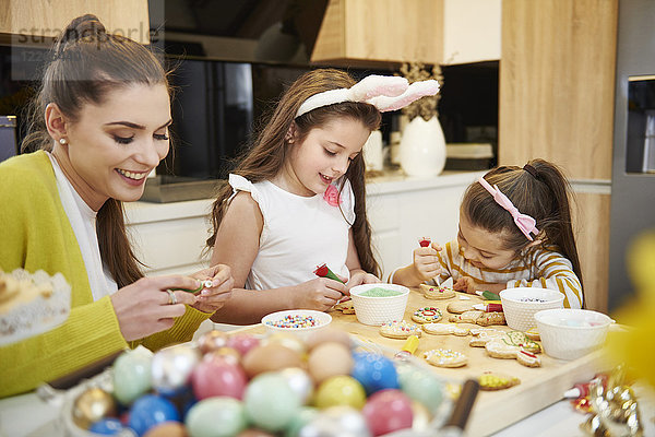 Mutter mit Töchtern  die Osterkekse in der Küche schmücken