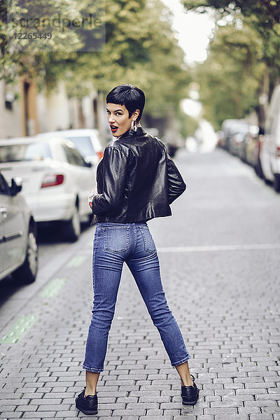 Modische junge Frau in Jeans und Lederjacke stehend auf der Straße