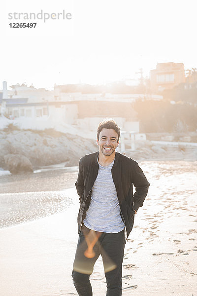 Porträt des lachenden jungen Mannes am Strand bei Dämmerung