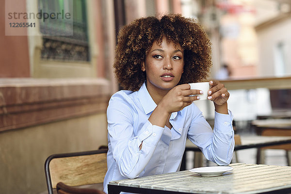 Frau mit Afro-Frisur sitzend im Outdoor-Café beim Kaffeetrinken