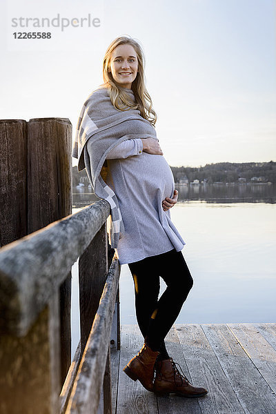 Porträt einer lächelnden  schwangeren Frau  die an einem See steht.