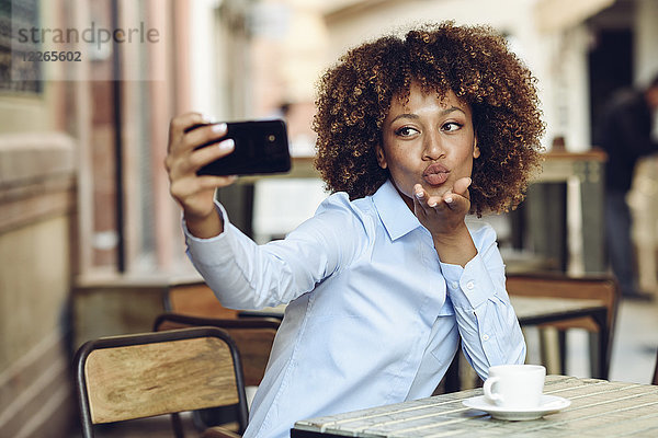 Frau mit Afro-Frisur sitzend im Outdoor-Café mit einem Selfie
