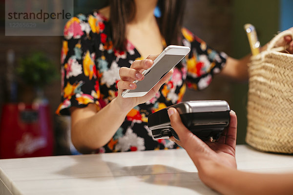 Nahaufnahme des bargeldlosen Bezahlens mit dem Smartphone am Schalter eines Ladens