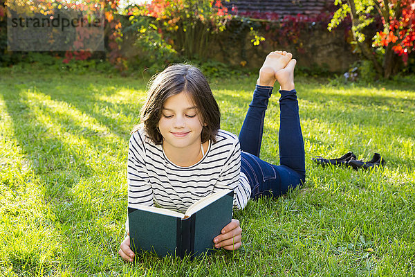 Lächelndes Mädchen liegt auf der Wiese und liest ein Buch.