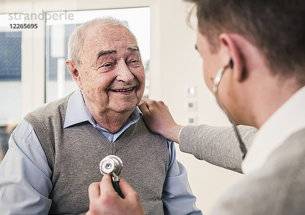 Älterer Mann lächelt Krankenschwester mit Stethoskop zu Hause an