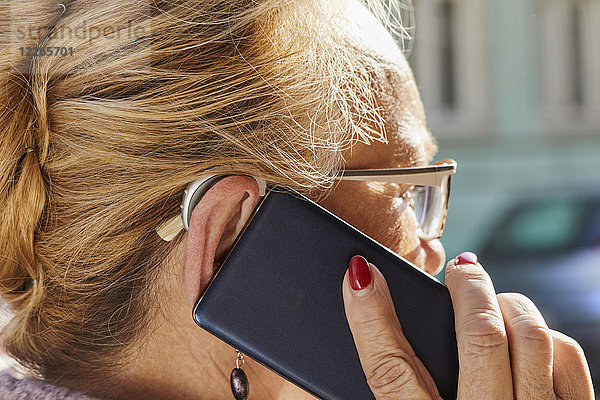 Nahaufnahme einer älteren Frau mit Hörgerät mittels Smartphone