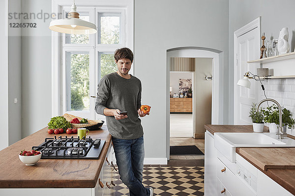 Mann mit Smartphone und Paprika in der Küche