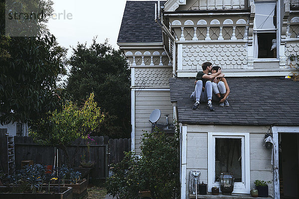 Paar auf dem Dach sitzend küssend