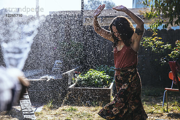Wasser spritzt auf junge Frau im Hinterhof