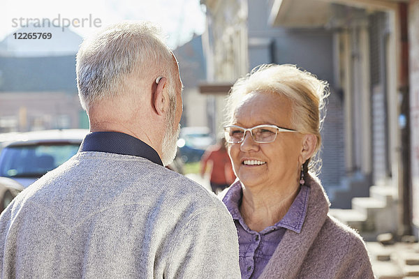 Nahaufnahme eines älteren Mannes mit Hörgerät im Gespräch mit einer älteren Frau