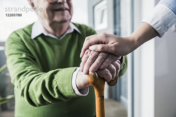 Nahaufnahme einer Frau  die die Hand eines älteren Mannes hält  der sich auf einen Stock stützt.