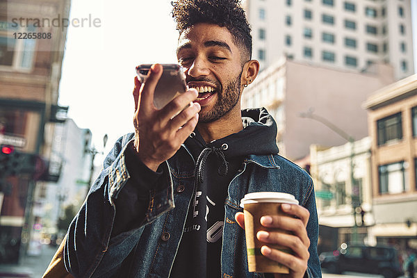 Porträt eines stilvollen jungen Mannes mit Kaffee und Smartphone auf der Straße