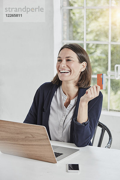 Lachende Geschäftsfrau mit Laptop auf Schreibtisch-Haltekarte