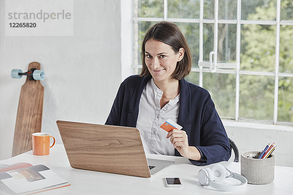 Porträt einer lächelnden Geschäftsfrau mit Laptop auf Schreibtisch-Haltekarte