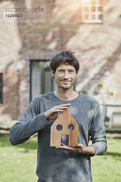 Porträt eines lächelnden Mannes vor seinem Haushaltenden Hausmodell