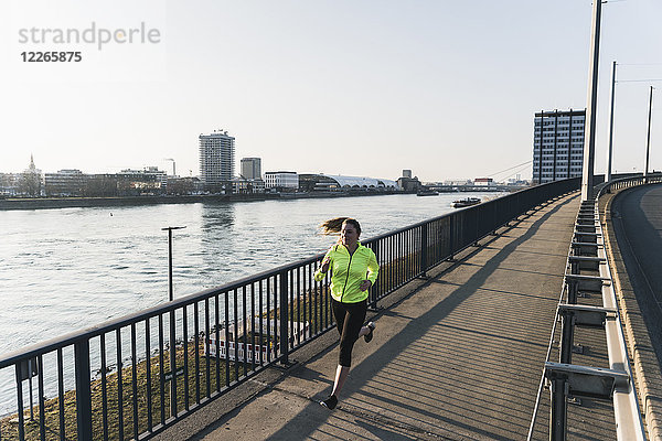 Junge Frau läuft auf Brücke am Flussufer