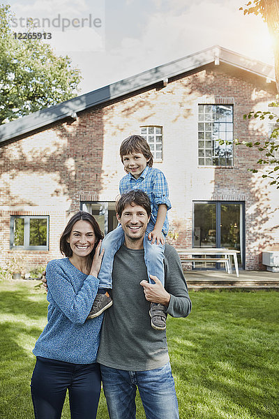 Porträt einer glücklichen Familie mit Sohn im Garten ihres Hauses