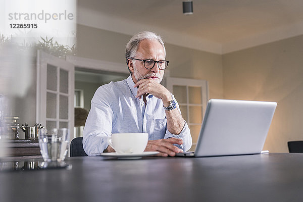 Porträt eines reifen Mannes  der am Tisch sitzt und den Laptop zu Hause benutzt.