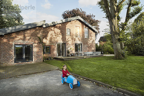 Mädchen spielt mit Seifenkiste in der Einfahrt des Wohnhauses