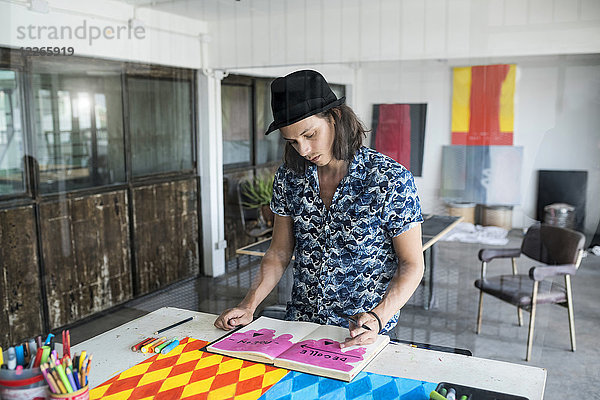 Künstler bei der Arbeit  Zeichnen in einem Notizbuch in seinem Loft-Atelier mit Bildern und Kunstwerken im Hintergrund.