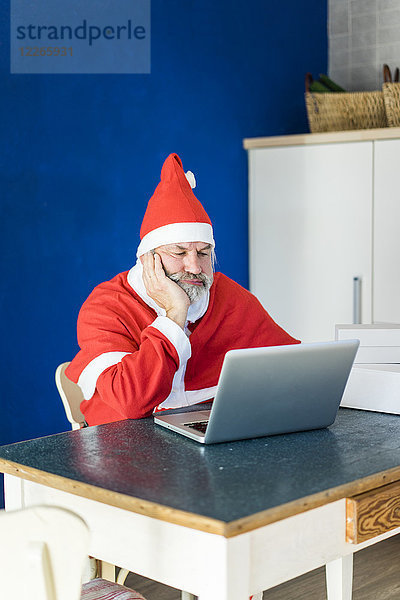 Frustrierte Weihnachtsmann mit Laptop zu Hause