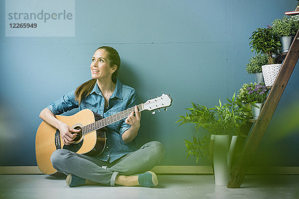 Frau entspannt in ihrem Haus mit Topfpflanzen  Gitarre spielen