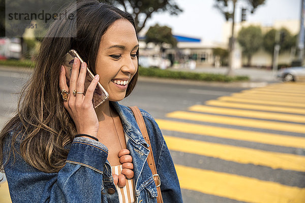 Lächelnde junge Frau spricht auf dem Smartphone auf der Straße