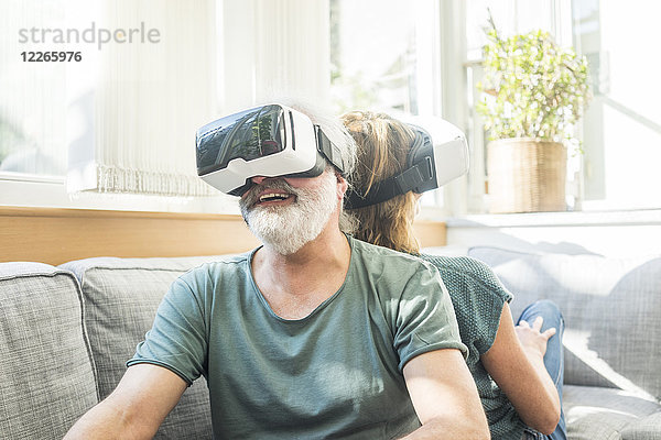 Glückliches reifes Paar  das zu Hause auf der Couch sitzt und eine VR-Brille trägt.