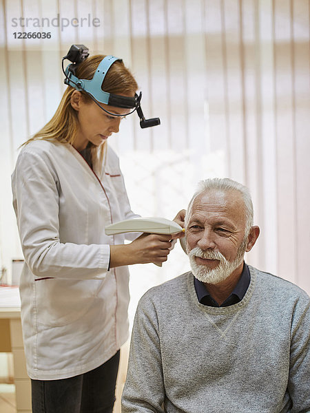 HNO-Arzt untersucht Ohr eines älteren Mannes