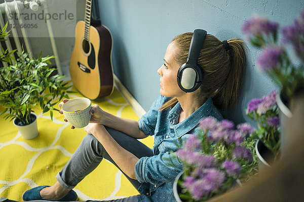 Schöne Frau in ihrem Haus  dekoriert mit Pflanzen  Musik hören mit Kopfhörern
