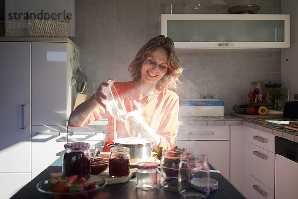 Lächelnde Frau macht Erdbeermarmelade in der Küche zu Hause
