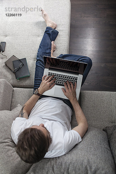 Mann auf der Couch zu Hause mit Laptop  Draufsicht