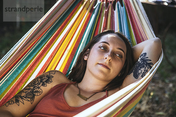 Portrait einer jungen Frau mit Tattoo in der Hängematte liegend