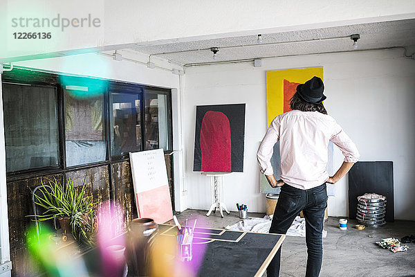 Künstler in seinem Loft-Atelier mit Blick auf seine Gemälde und Kunstwerke