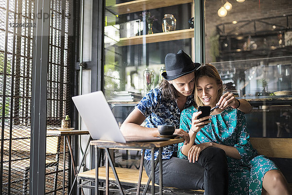 Künstlerpaar sitzt im Café und überprüft das Smartphone der jungen Frau