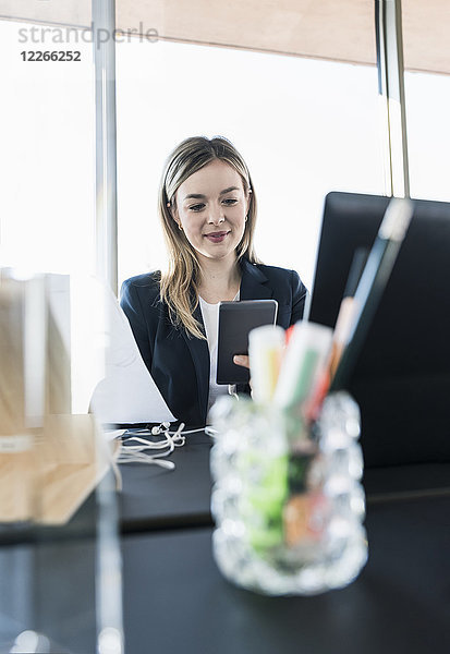Lächelnde junge Geschäftsfrau mit Handy am Schreibtisch im Büro