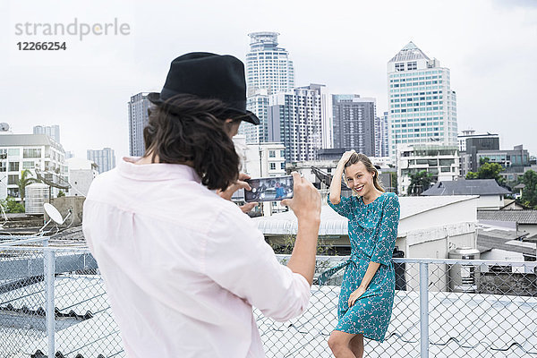 TYoung Mann mit Smartphone beim Fotografieren der Freundin auf dem Dach