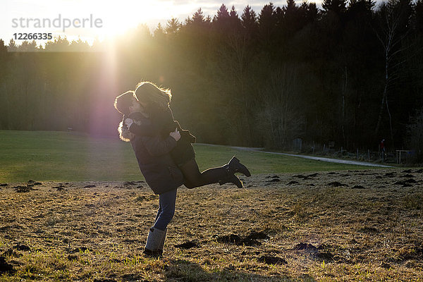 Glückliches junges Paar  das sich auf dem Feld gegen die Sonne küsst.