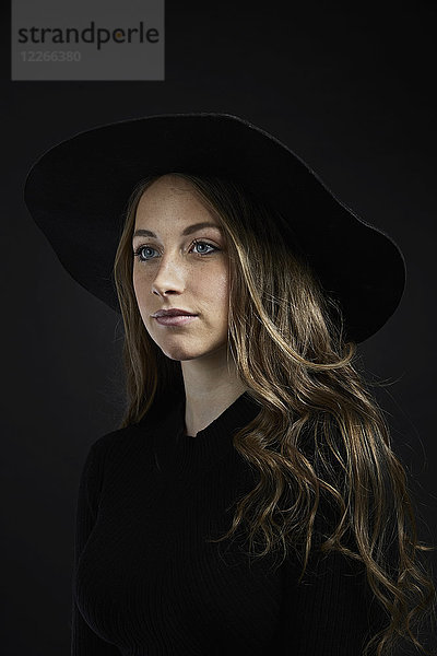 Porträt einer jungen Frau mit schwarzem Hut und Kleidung vor schwarzem Hintergrund